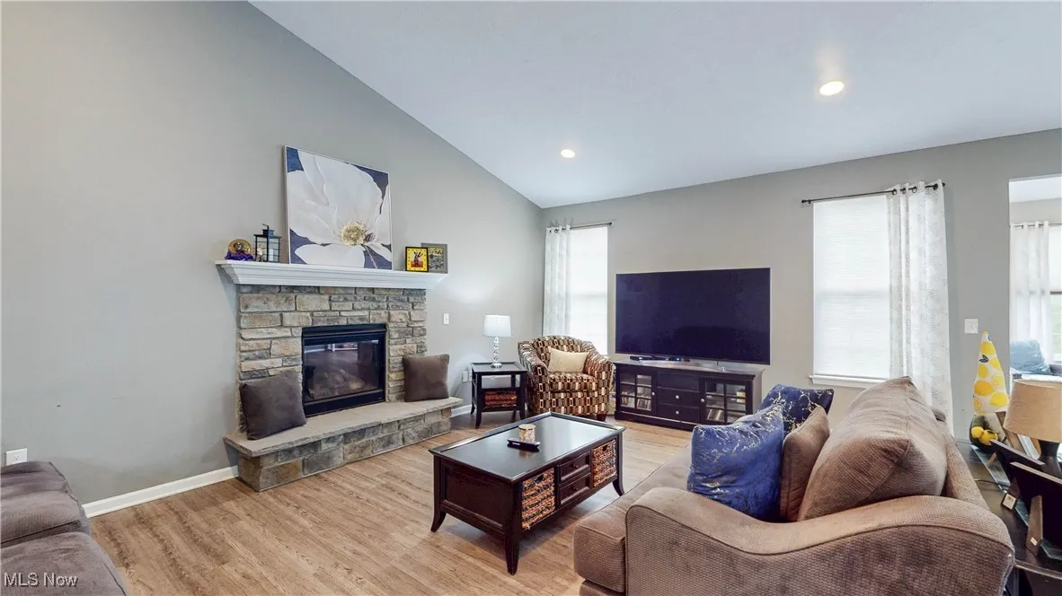 Great room featuring natural light, a fireplace, light wood-type flooring, vaulted ceiling, and recessed lighting