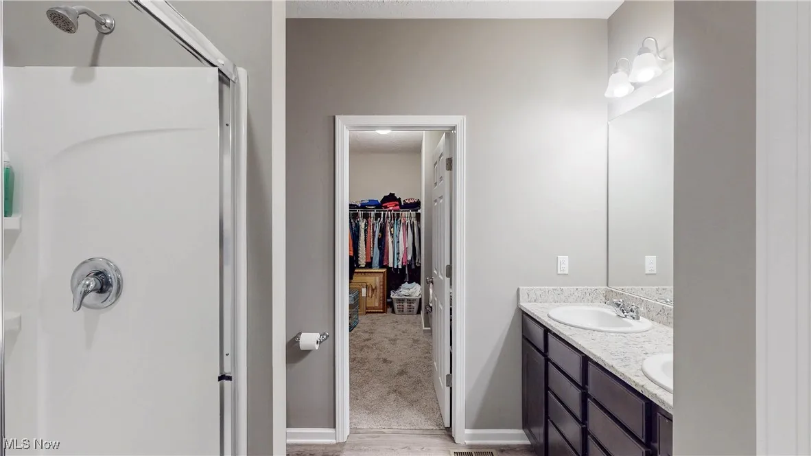 Bathroom with double vanity, a spacious closet, a shower, and light wood-style floors
