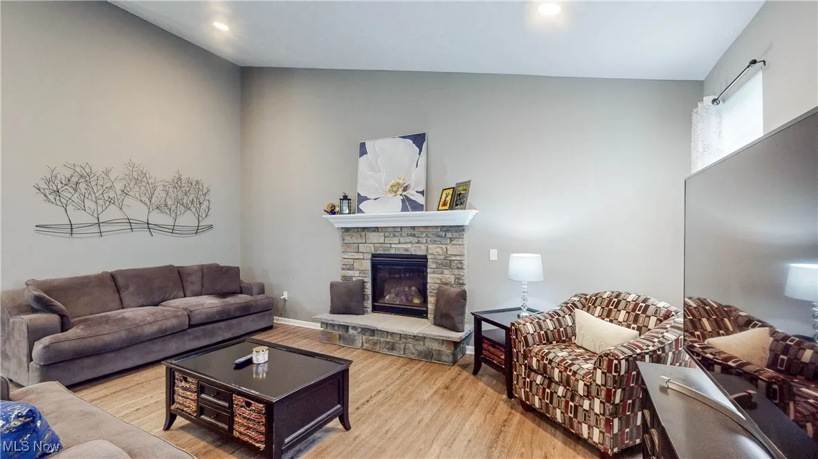 Great room featuring wood finished floors, a stone fireplace, vaulted ceiling, and recessed lighting