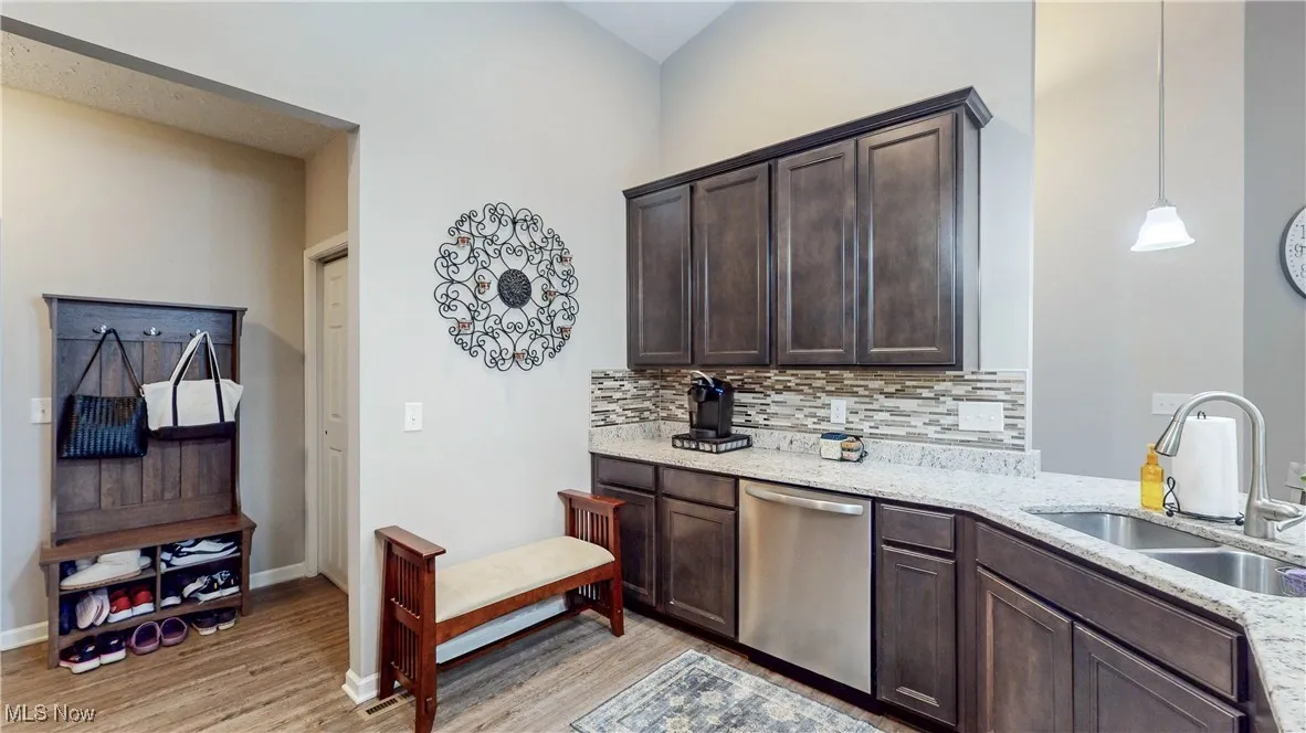 Kitchen with dark brown cabinetry, light stone countertops, dishwasher, and light wood-type flooring