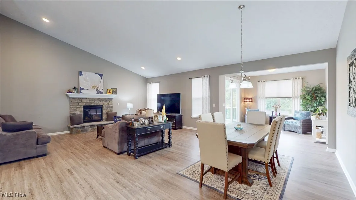 Dining space featuring light wood finished floors, vaulted ceiling, a stone fireplace, recessed lighting, and a chandelier