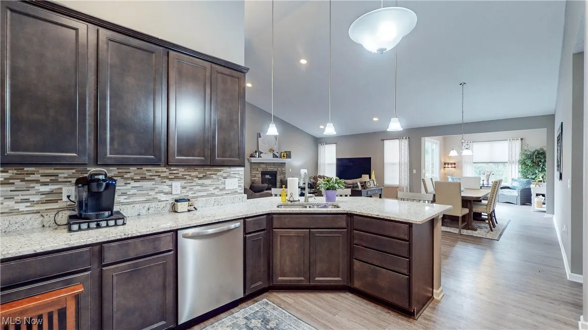 Kitchen with dark brown cabinets, pendant lighting, dishwasher, light stone counters, and light wood-style floors