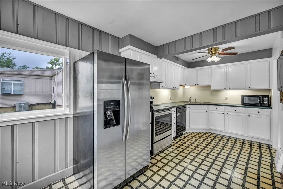 Kitchen with black appliances, dark countertops, white cabinets, inlaid floor details, and ceiling fan