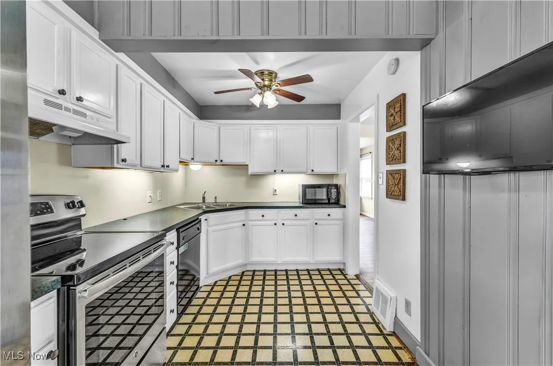 Kitchen with black appliances, under cabinet range hood, ceiling fan, white cabinets, and dark countertops