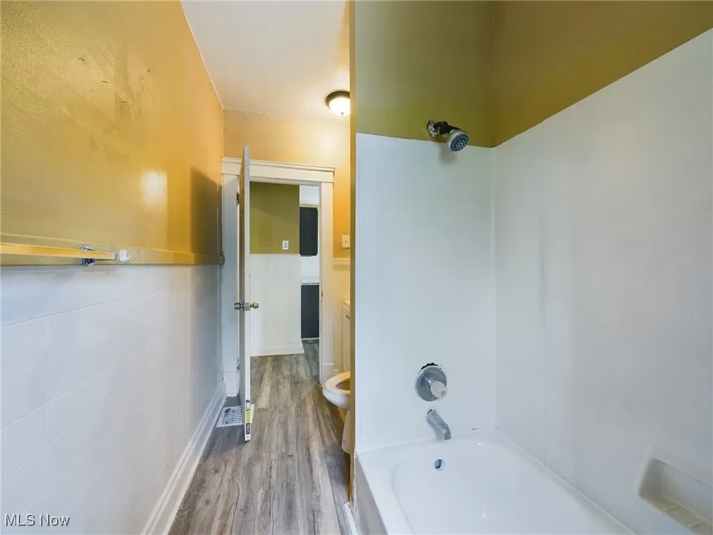 Full bathroom featuring shower / bath combination, dark wood-type flooring, and a wainscoted wall