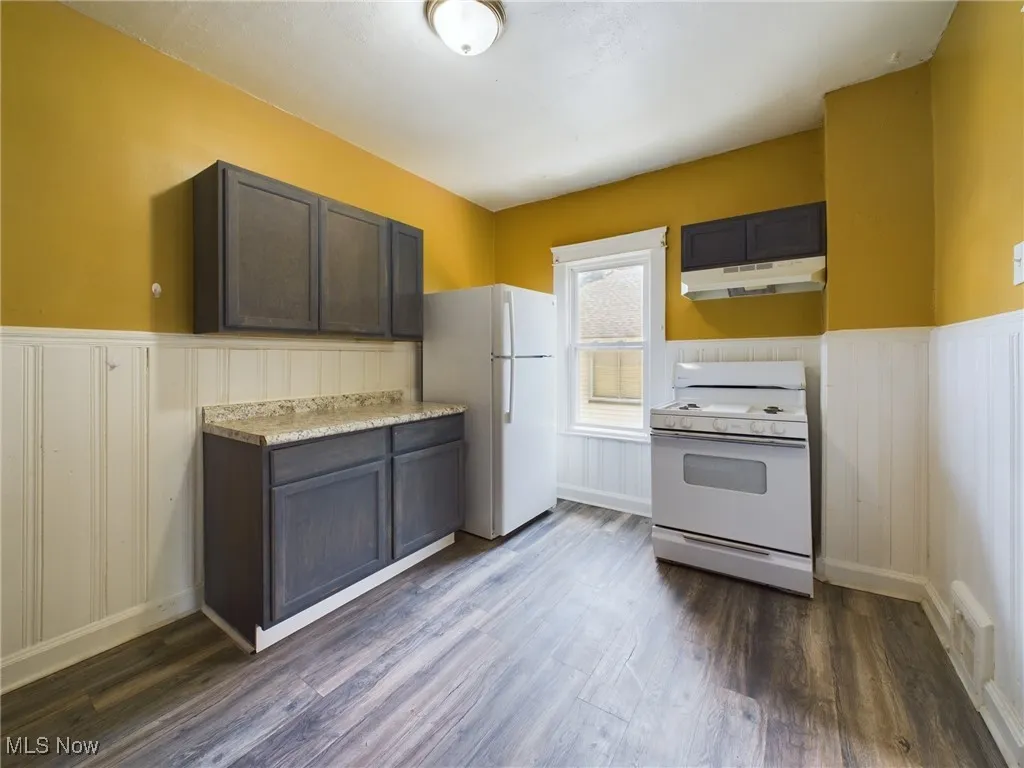 Kitchen with wainscoting, light countertops, white appliances, dark brown cabinetry, and under cabinet range hood