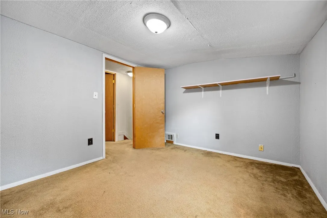 Empty room featuring a textured ceiling, carpet flooring, and a textured wall