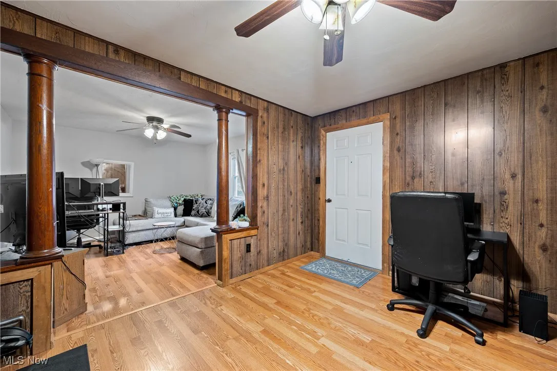Home office featuring decorative columns, wood walls, a ceiling fan, and light wood finished floors