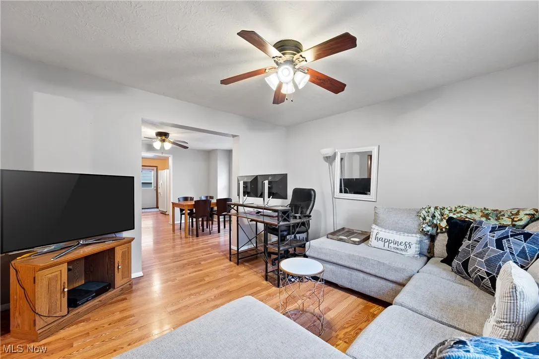 Living room featuring light wood finished floors, a ceiling fan, and a textured ceiling