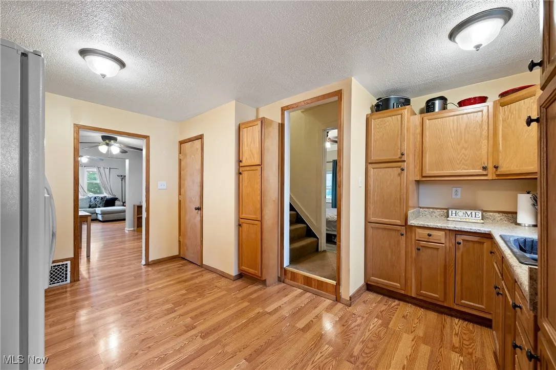 Kitchen with light wood-style floors, freestanding refrigerator, a textured ceiling, a ceiling fan, and brown cabinetry