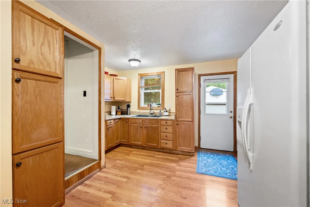 Kitchen featuring white refrigerator with ice dispenser, a textured ceiling, light countertops, light wood-style floors, and brown cabinets