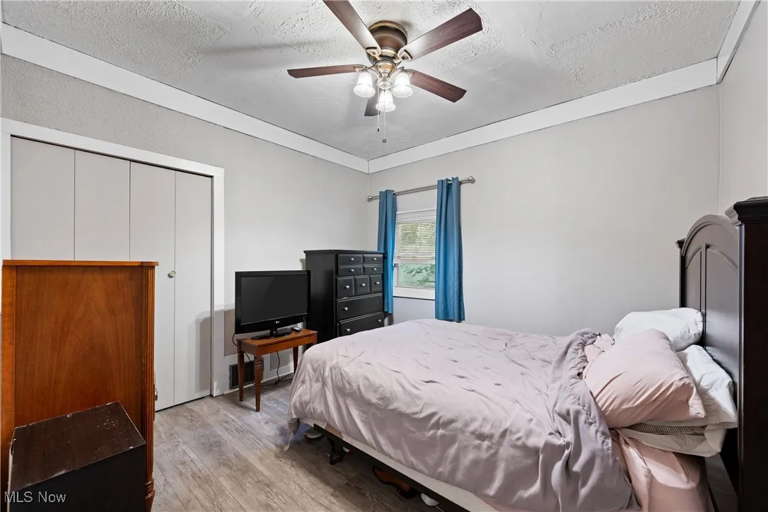 Bedroom with light wood-style floors, ceiling fan, a closet, and a textured ceiling