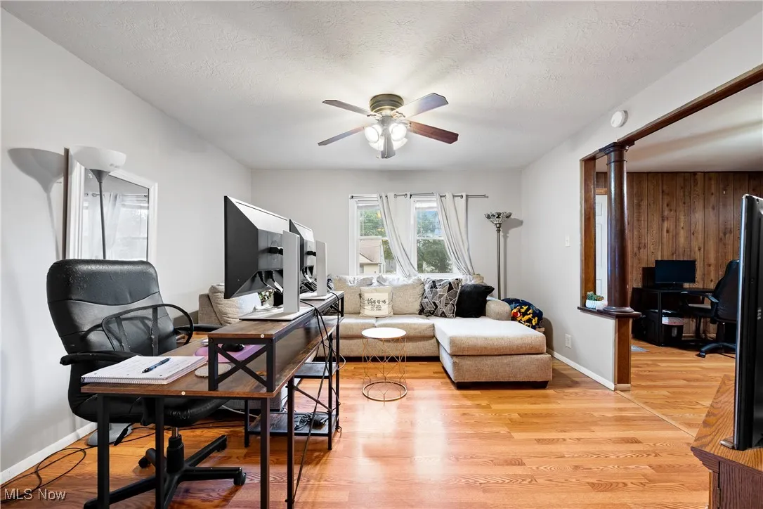 Living room featuring a desk, light wood-style floors, a textured ceiling, ceiling fan, and wood walls
