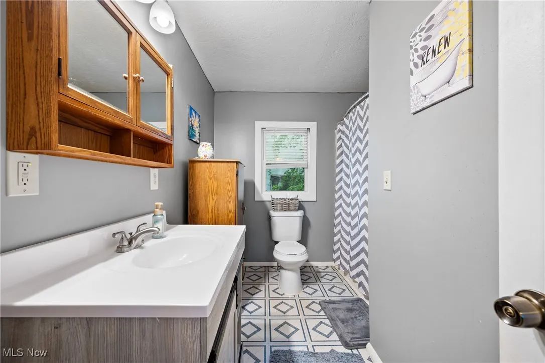 Full bathroom with vanity, a textured ceiling, a shower with curtain, and light tile patterned floors