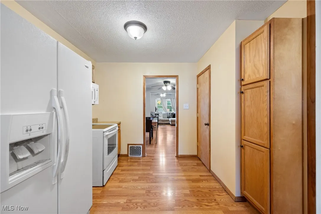 Kitchen featuring white appliances, a textured ceiling, light wood finished floors, light countertops, and ceiling fan