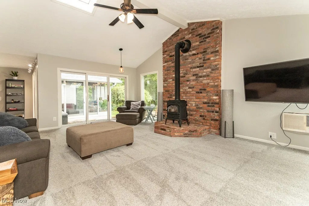 Living area featuring a wood stove, carpet, beamed ceiling, a ceiling fan, and high vaulted ceiling