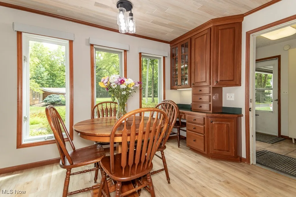 Dining space with light wood finished floors, built in desk, wooden ceiling, and crown molding