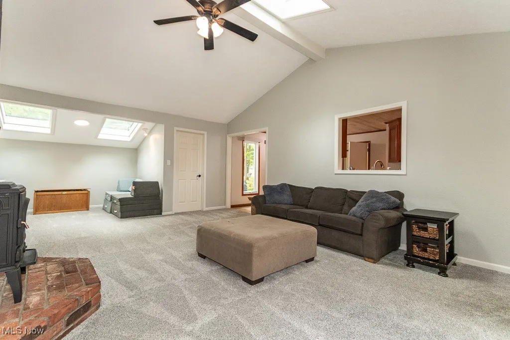 Carpeted living room featuring a skylight, a wood stove, and a ceiling fan