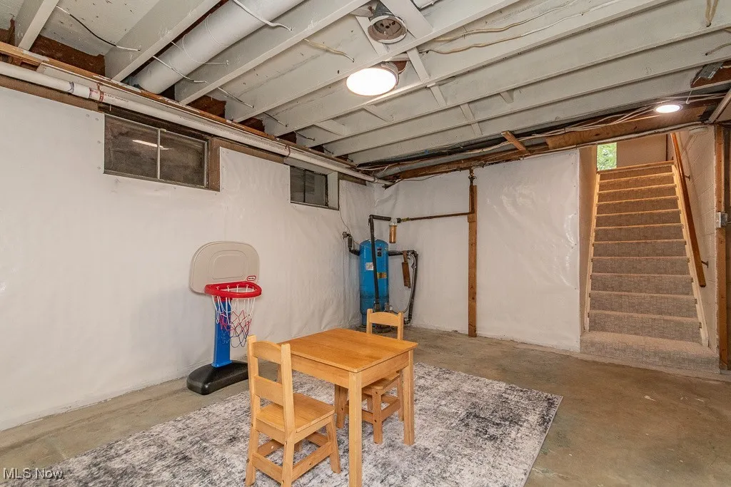 Unfinished below grade area featuring a water pressure tank and stairway