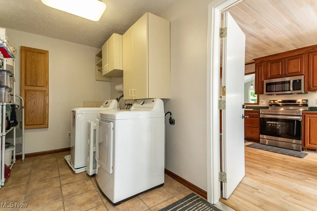 Washroom featuring independent washer and dryer, a textured ceiling, cabinet space, and light tile patterned floors