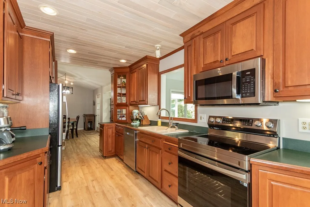 Kitchen with appliances with stainless steel finishes, brown cabinetry, light wood finished floors, recessed lighting, and dark countertops