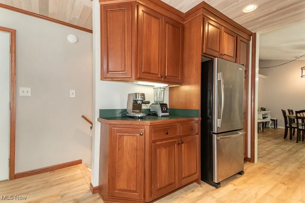 Kitchen with freestanding refrigerator, light wood-style floors, brown cabinetry, and dark countertops