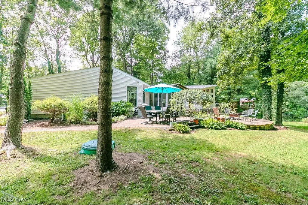 View of green lawn with a patio and view of wooded area