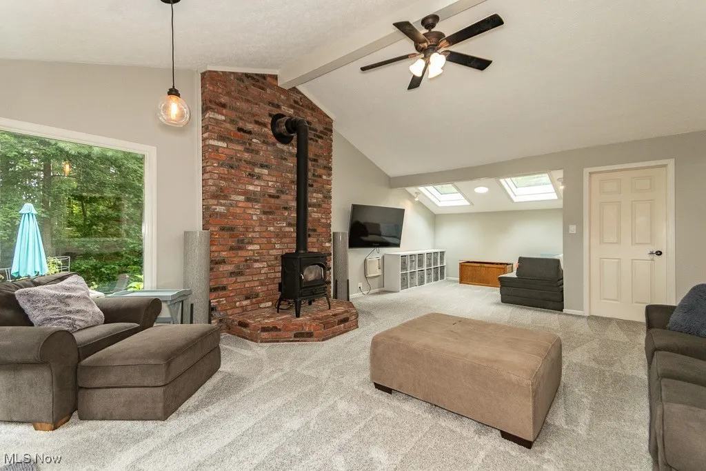 Living room with carpet floors, a skylight, a wood stove, and a ceiling fan