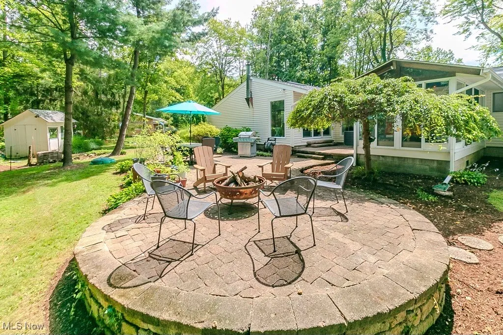 View of patio with a fire pit, view of wooded area, area for grilling, and a storage unit