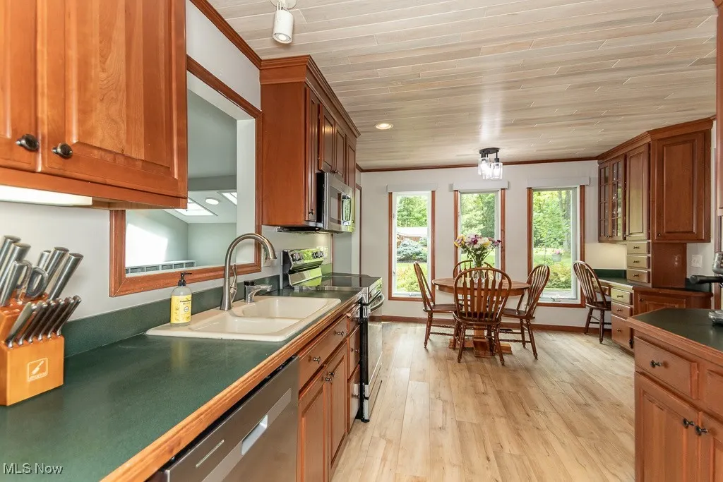 Kitchen featuring appliances with stainless steel finishes, light wood finished floors, wooden ceiling, brown cabinetry, and dark countertops