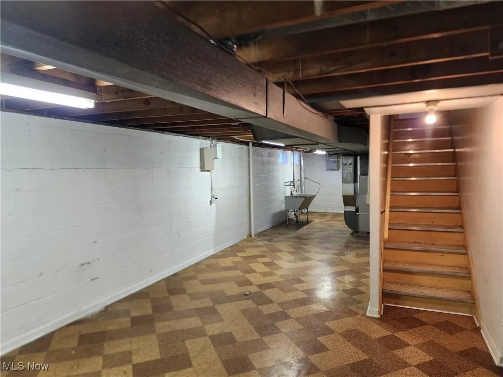 Unfinished basement featuring tile patterned floors, stairway, heating unit, and electric panel