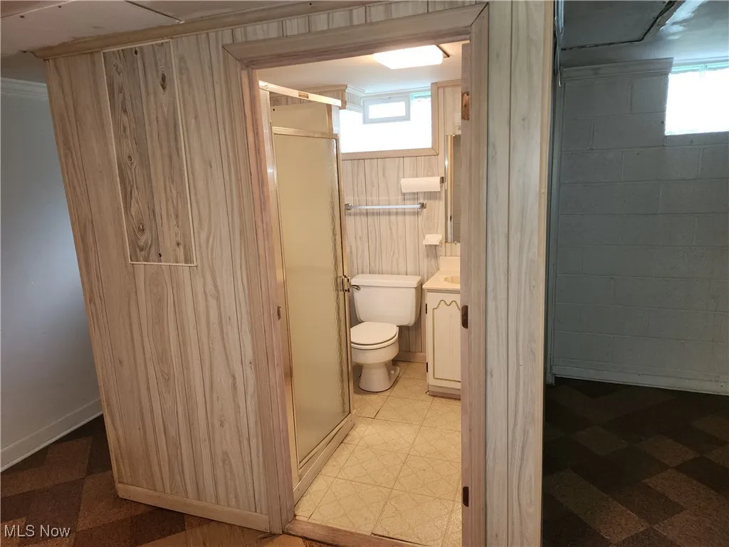 Bathroom with a stall shower, vanity, light floors, and wooden walls