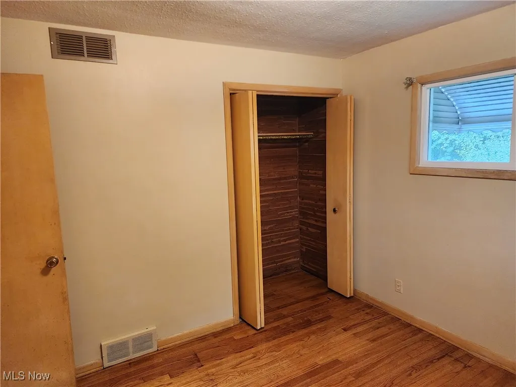 Unfurnished bedroom featuring wood finished floors, a textured ceiling, and a closet