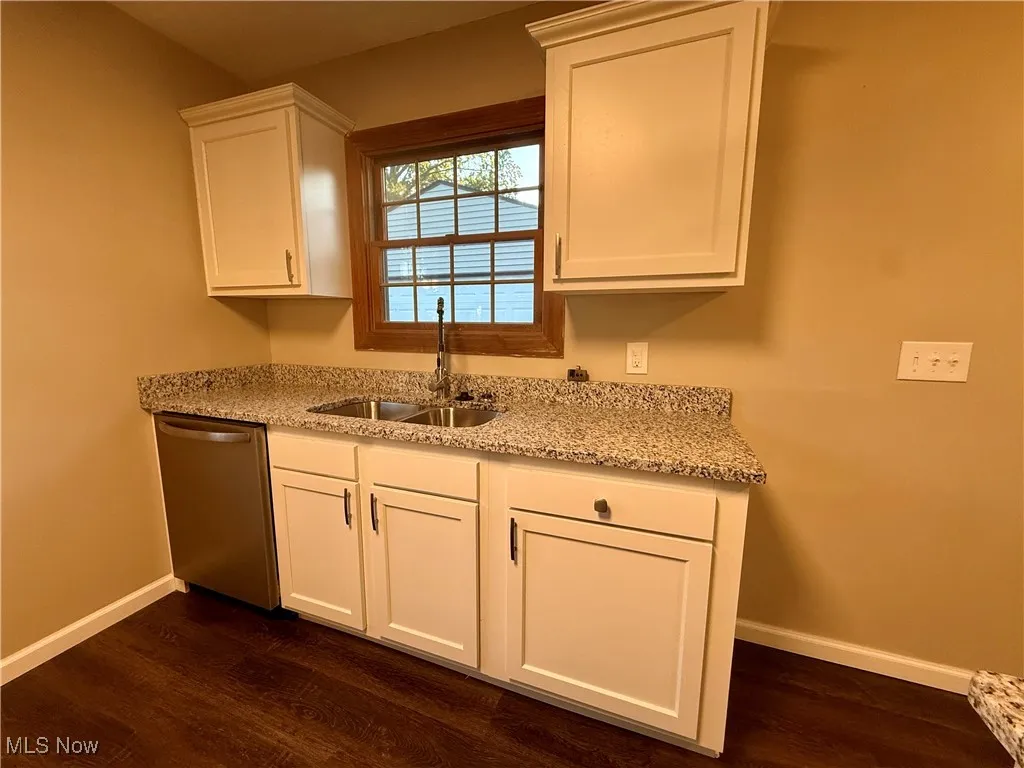 Kitchen featuring light stone countertops, white cabinets, stainless steel dishwasher, and dark wood-style flooring