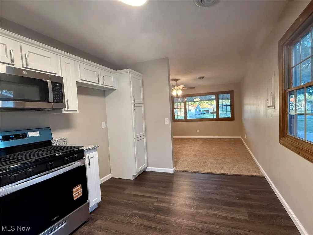 Kitchen featuring gas range, white cabinets, stainless steel microwave, and dark wood finished floors