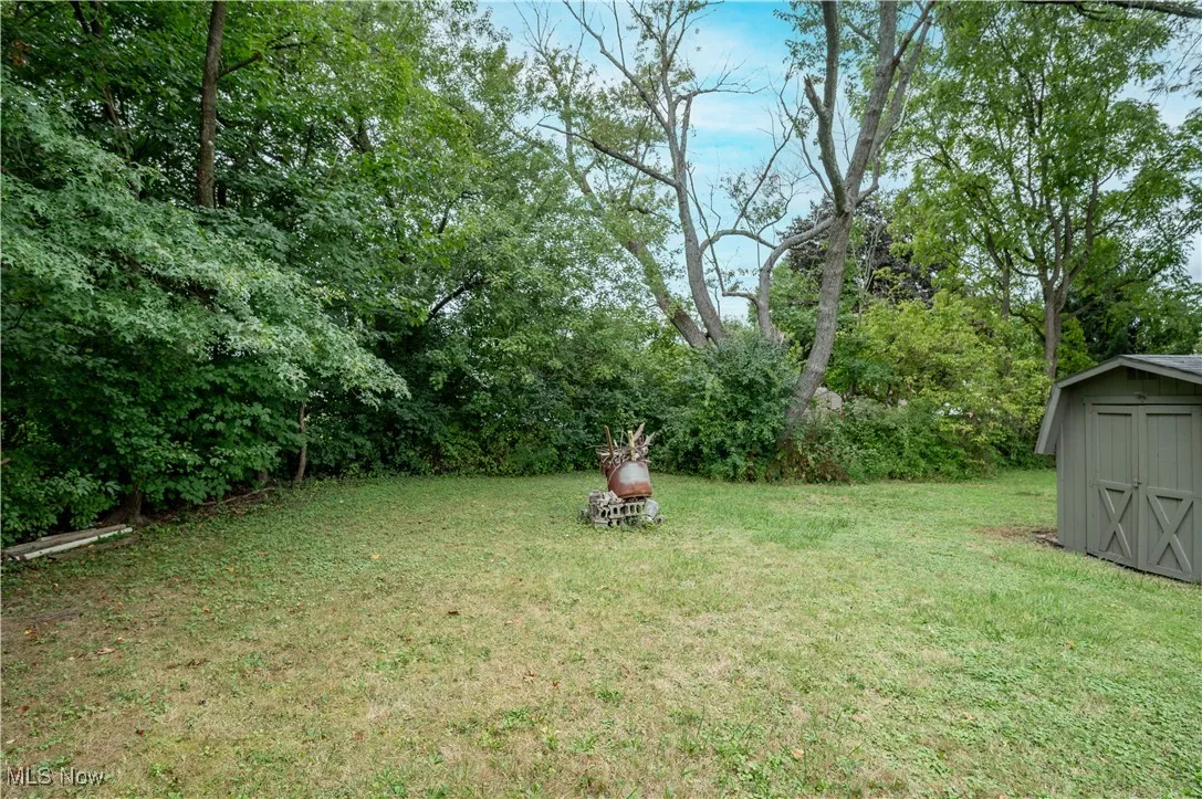 View of grassy yard featuring a storage unit and view of wooded area