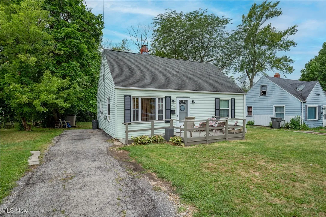 Cape cod house featuring a front yard, a deck, a shingled roof, a chimney, and asphalt driveway