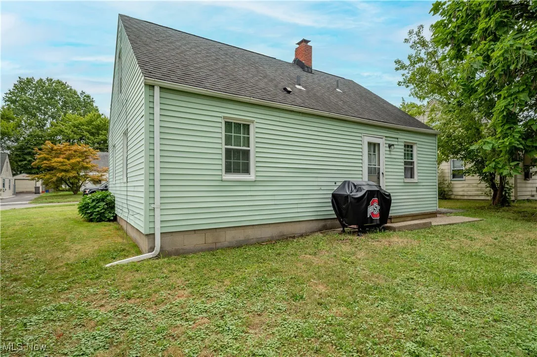 Rear view of property with a chimney, a lawn, and roof with shingles
