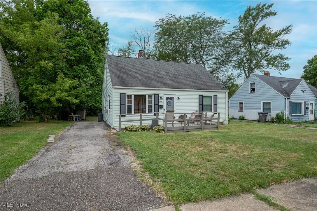 Cape cod house with a deck, roof with shingles, a chimney, a front yard, and driveway