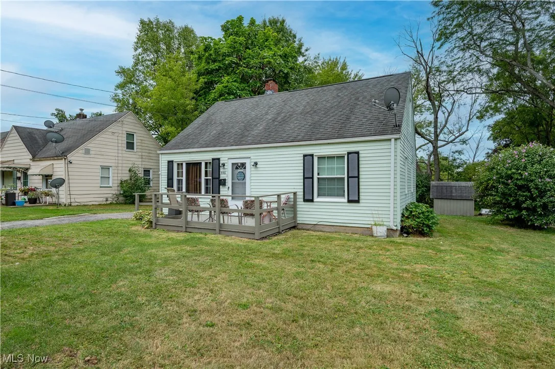 Cape cod-style house with a wooden deck, a storage shed, a front yard, a chimney, and a shingled roof