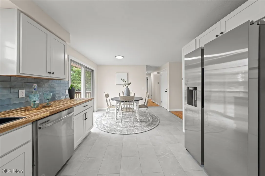 Kitchen featuring appliances with stainless steel finishes, white cabinets, butcher block counters, backsplash, and light tile patterned flooring