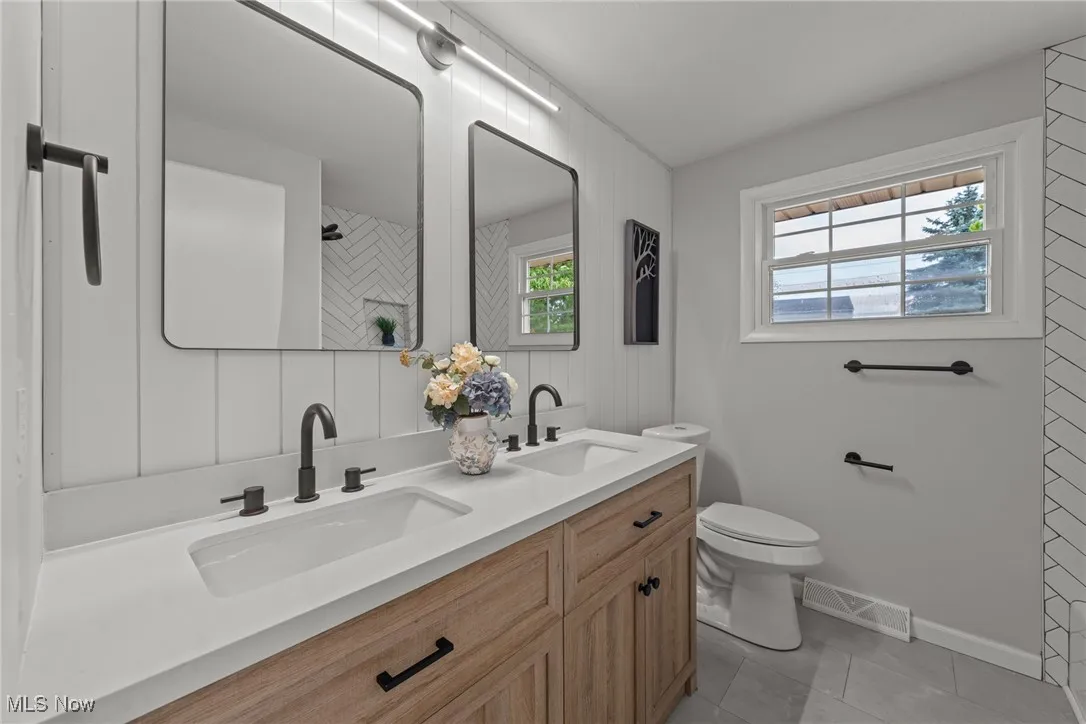 Bathroom featuring healthy amount of natural light, double vanity, light tile patterned floors, and a shower