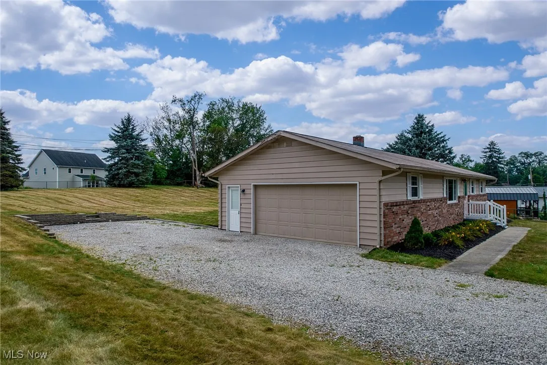 View of home's exterior with brick siding, a yard, a garage, and gravel driveway