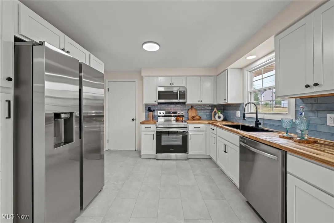 Kitchen with appliances with stainless steel finishes, backsplash, white cabinetry, light tile patterned flooring, and butcher block countertops