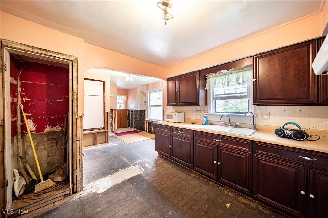 Kitchen with dark brown cabinets, light countertops, decorative backsplash, and white microwave