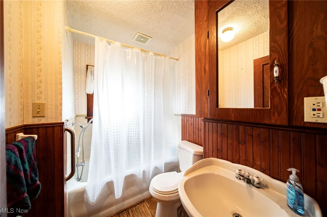 Full bathroom with shower / tub combo, a textured ceiling, and wallpapered walls