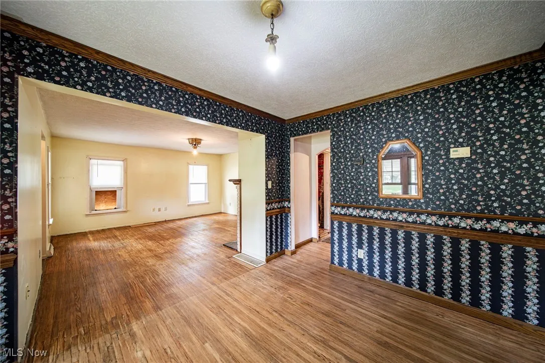 Unfurnished room featuring wallpapered walls, ornamental molding, wood finished floors, and a textured ceiling