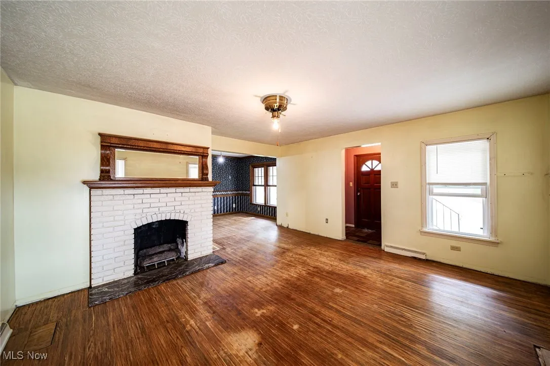 Unfurnished living room featuring a fireplace, wood finished floors, a textured ceiling, and baseboard heating