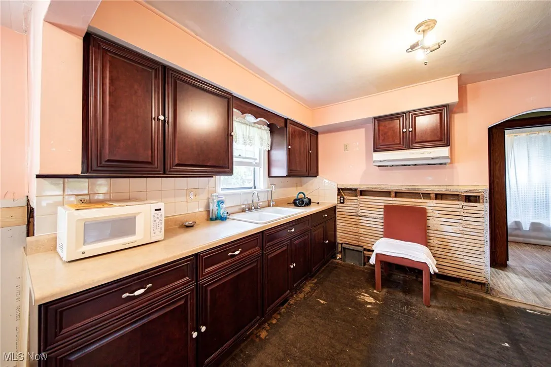 Kitchen with light countertops, decorative backsplash, white microwave, dark brown cabinetry, and under cabinet range hood