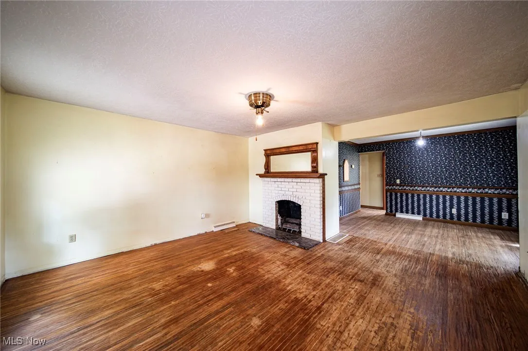 Unfurnished living room with wallpapered walls, a fireplace, dark wood-style floors, and a textured ceiling